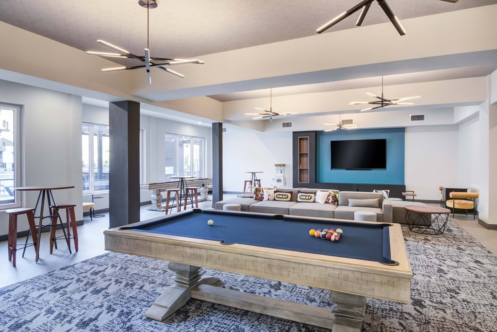 The Beacon game room lounge with billiards table, shuffleboard, arcade table, couches, high top tables, and a wall mounted tv
