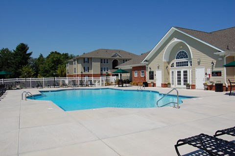 A large swimming pool in front of a building with a white fence and trees in the background.