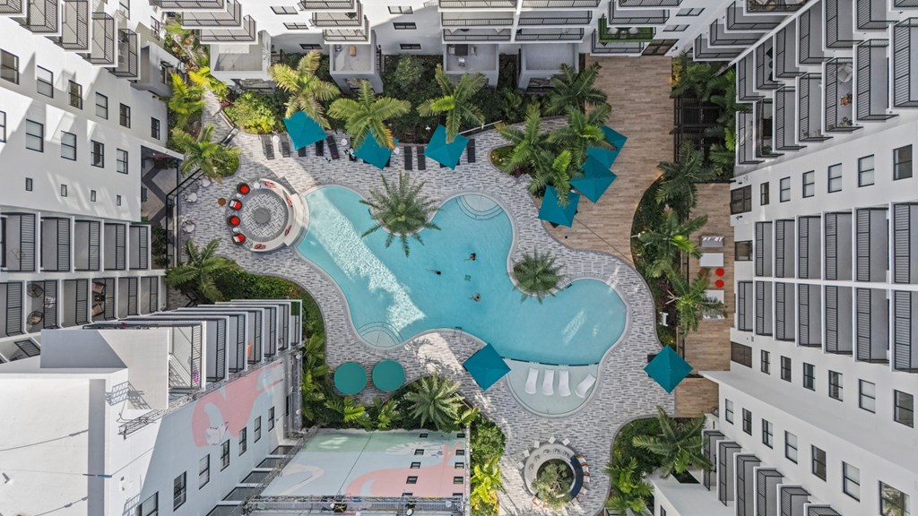 A pool surrounded by palm trees and a white building.