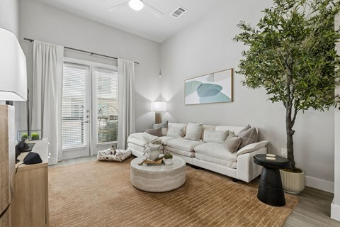 A living room with a white couch, a tree, and a painting on the wall.