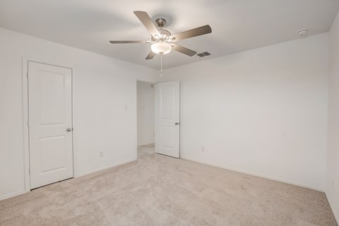 Generous bedroom space with carpet flooring and a central ceiling fan for added comfort and circulation
