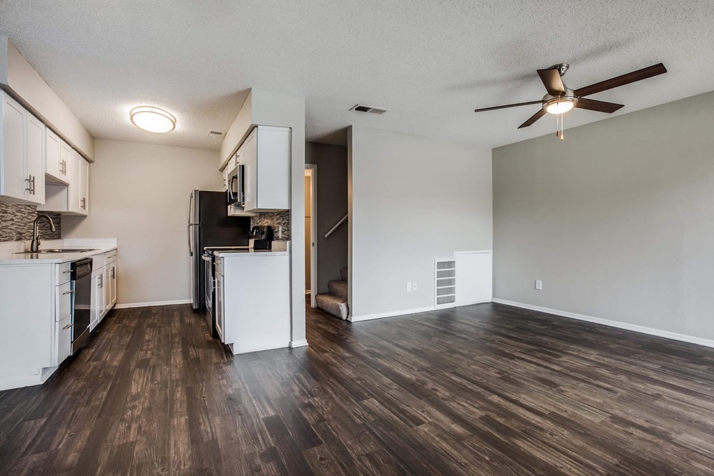 an empty living room with a kitchen and a ceiling fan
