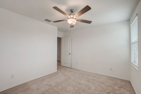 Generous bedroom space with carpet flooring and a central ceiling fan for added comfort and circulation.