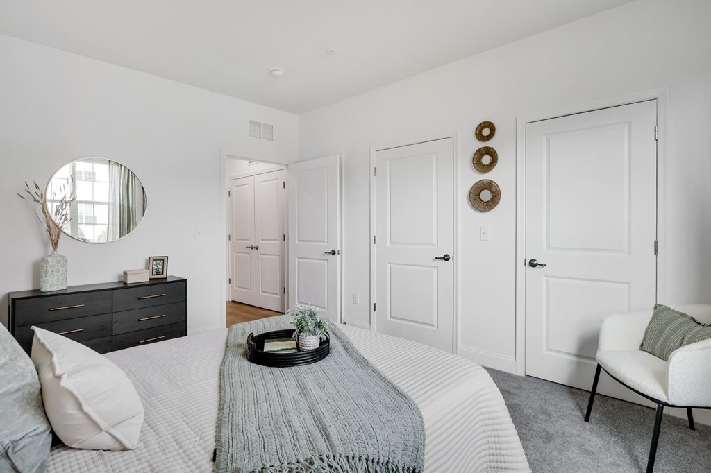 A bedroom with a bed, a chair, and a dresser with a mirror.