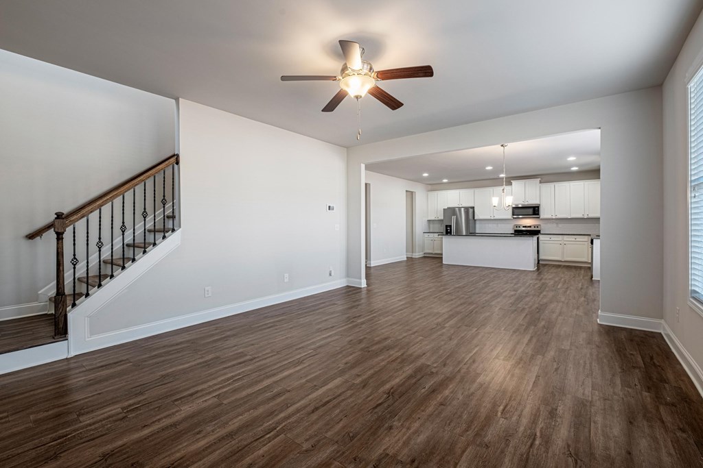 an empty living room with a ceiling fan and a kitchen