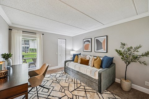 A living room with a grey couch, a wooden table, a rug and a potted plant.