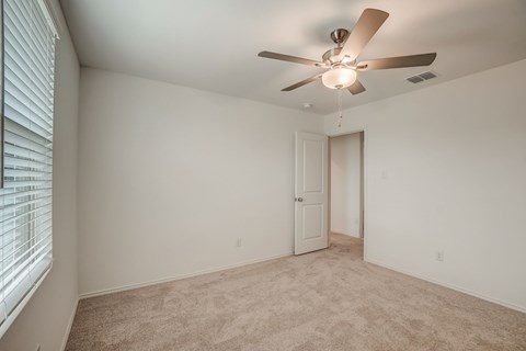 Generous bedroom space with carpet flooring and a central ceiling fan for added comfort and circulation