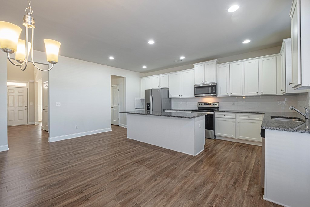 an open kitchen and living room with white cabinets and wood floors