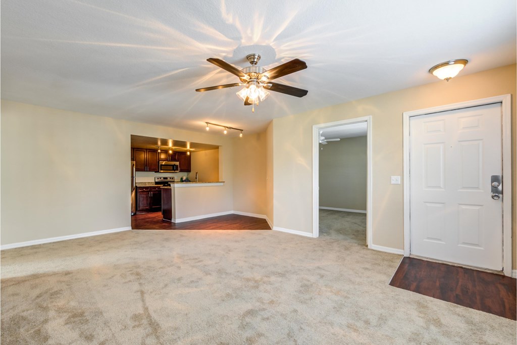 a empty living room with a ceiling fan and a kitchen