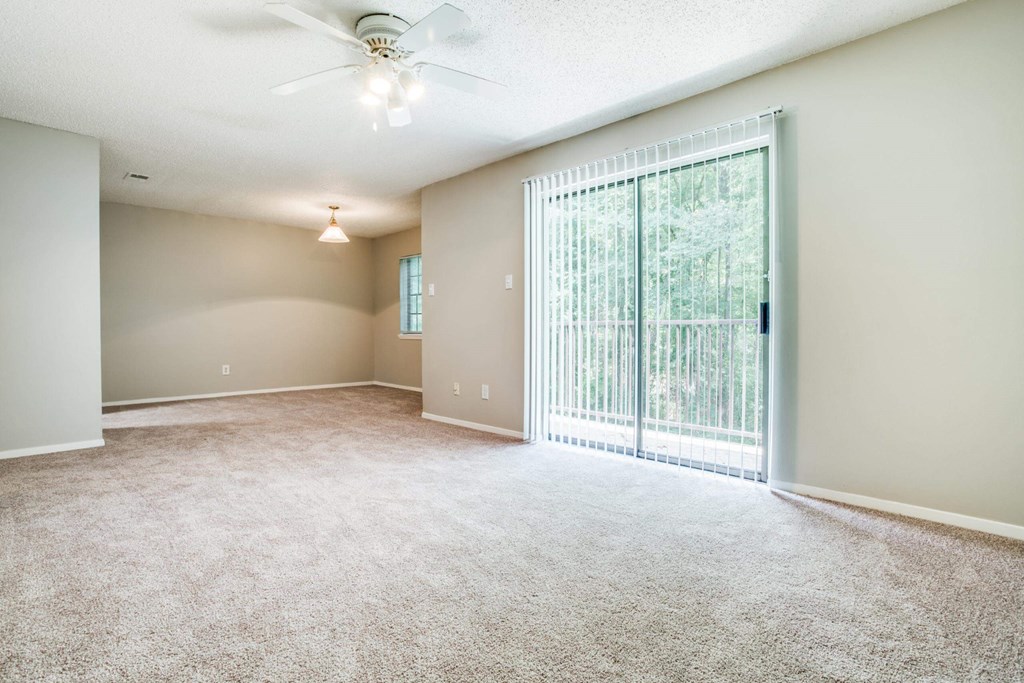 an empty living room with a large window and a ceiling fan