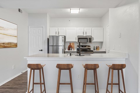 A kitchen with white cabinets and a white countertop with three bar stools.