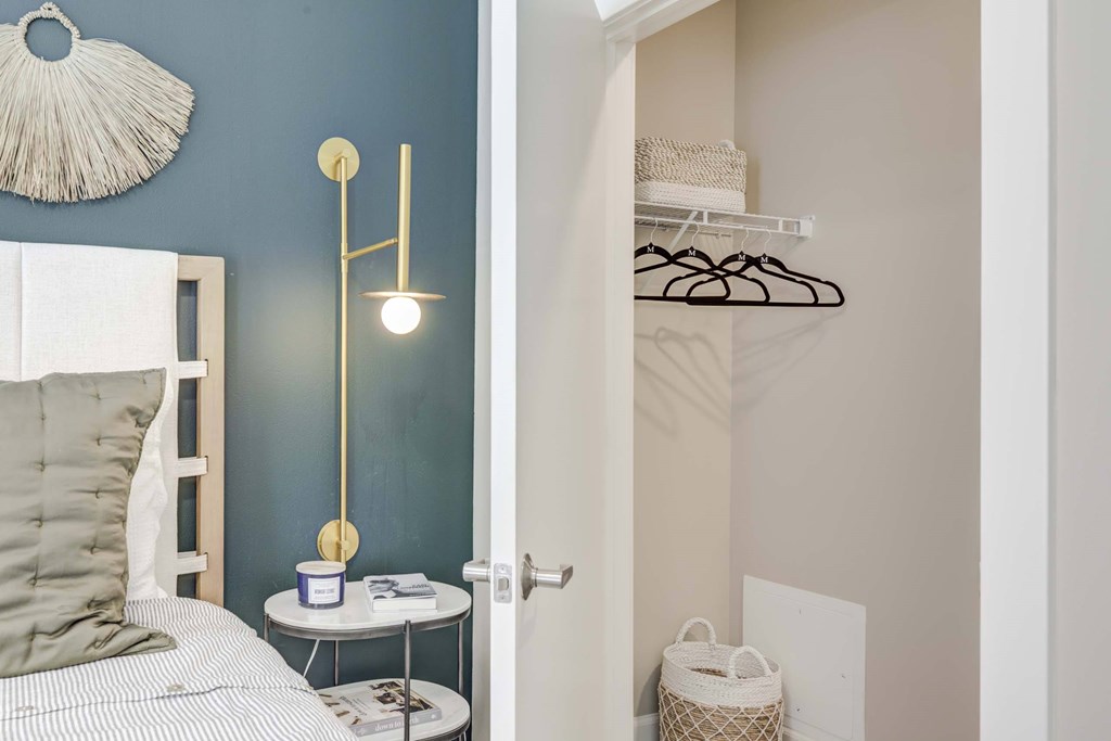 A bedroom with a bed, a nightstand with a lamp, and a closet with clothes.