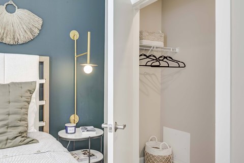 A bedroom with a bed, a nightstand with a lamp, and a closet with clothes.