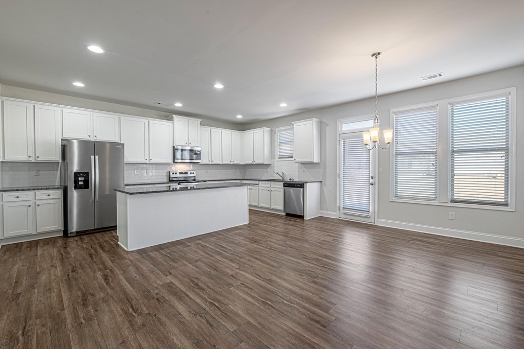 an open kitchen and living room with white cabinets and stainless steel appliances