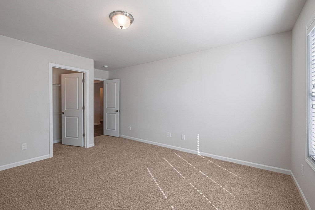 an empty living room with carpet and a door to a hallway