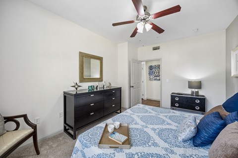 A bedroom with a blue patterned bedspread and a ceiling fan.