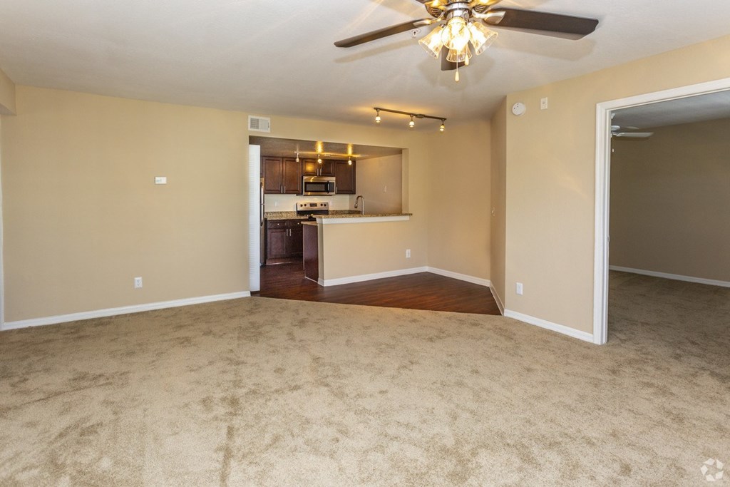 an empty living room with a kitchen in the background