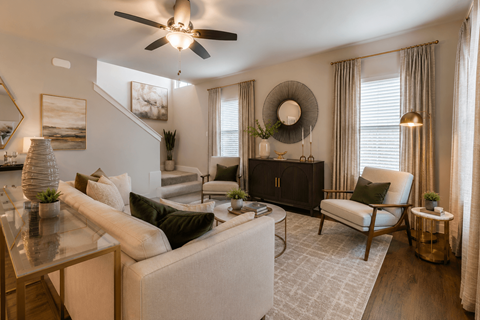 A living room with a white couch, a glass table, a ceiling fan, and a staircase.