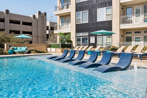 A row of blue lounge chairs are arranged around a swimming pool.