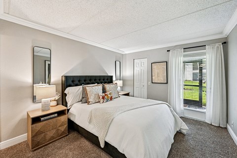 A bedroom with a large bed and a window with white curtains.