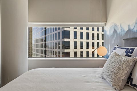 A bedroom with a large bed and a window with a view of a cityscape.