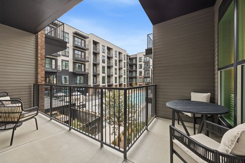 A balcony with a table and chairs overlooks a pool.