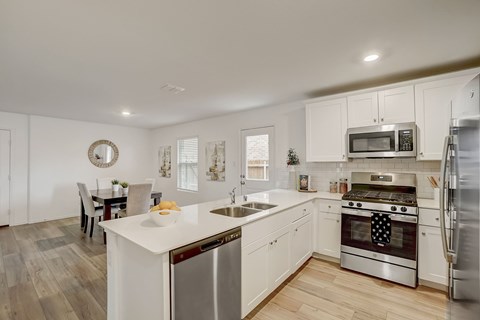 Spacious L-Shaped Kitchen with white cabinetry, giving way to the dining room, all over hardwood floor