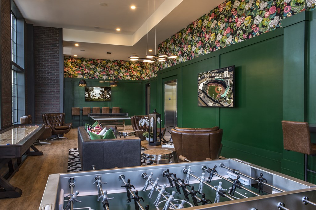 A foosball table is in the middle of a room with green walls and a floral wallpaper border.