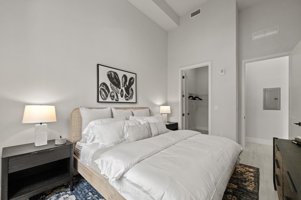 A bedroom with a large bed, two lamps, and a painting on the wall.