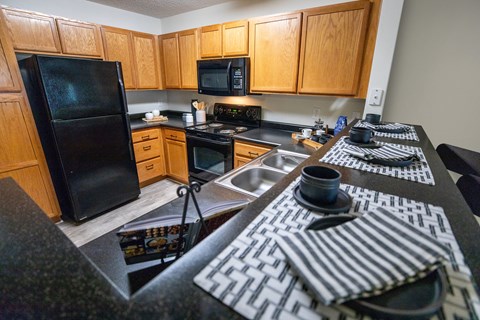 A black refrigerator is in a kitchen with wooden cabinets.