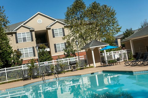 A swimming pool in front of a house with a white picket fence.