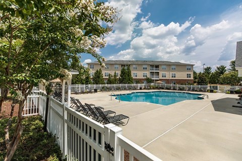A pool surrounded by a white fence with trees in the foreground.