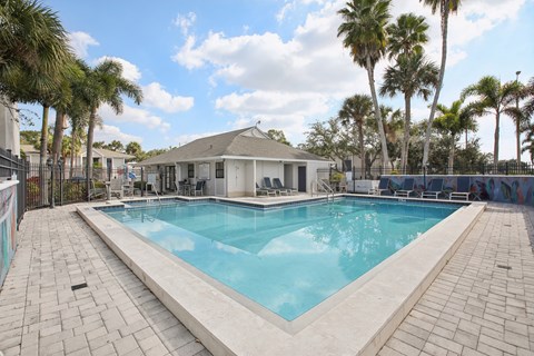 A pool surrounded by palm trees and a white building.
