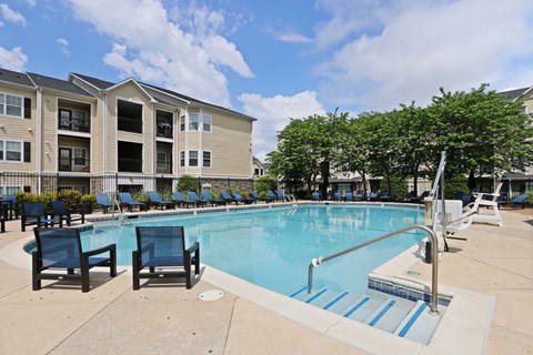 A swimming pool surrounded by chairs and trees in front of a building.