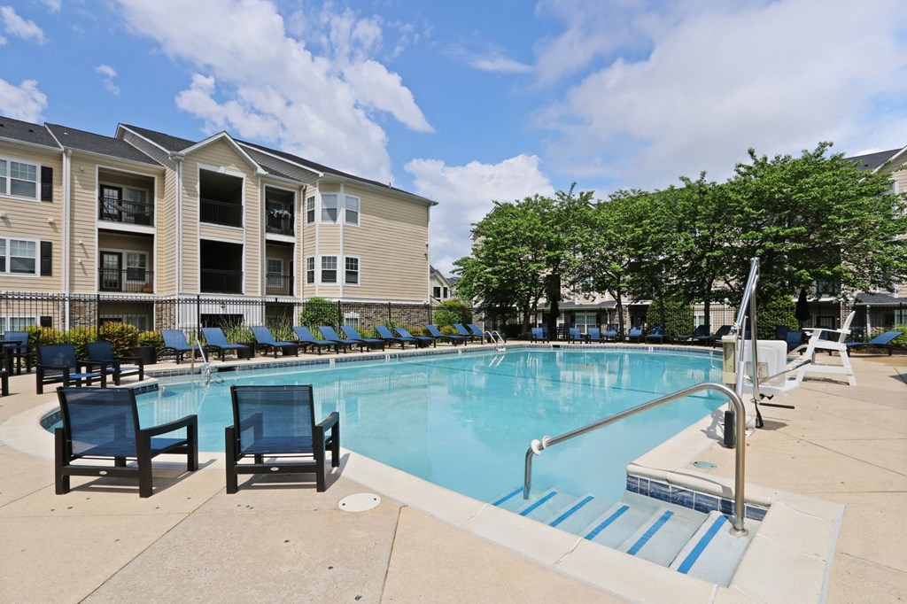 A swimming pool surrounded by chairs and trees in front of a building.