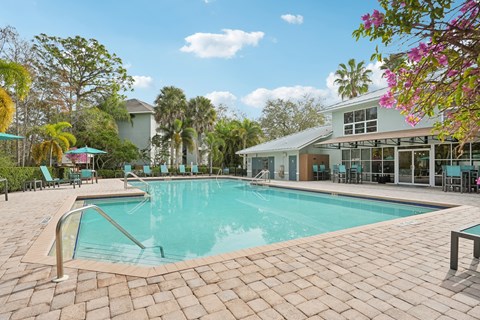 A large outdoor swimming pool surrounded by a brick patio and lounge chairs.