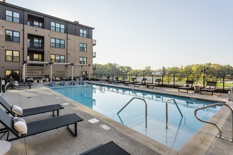 A large swimming pool with lounge chairs and a building in the background.