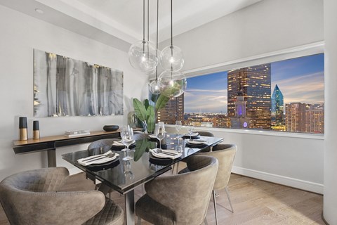 A modern dining room with a glass table and chairs, a chandelier, and a cityscape view.