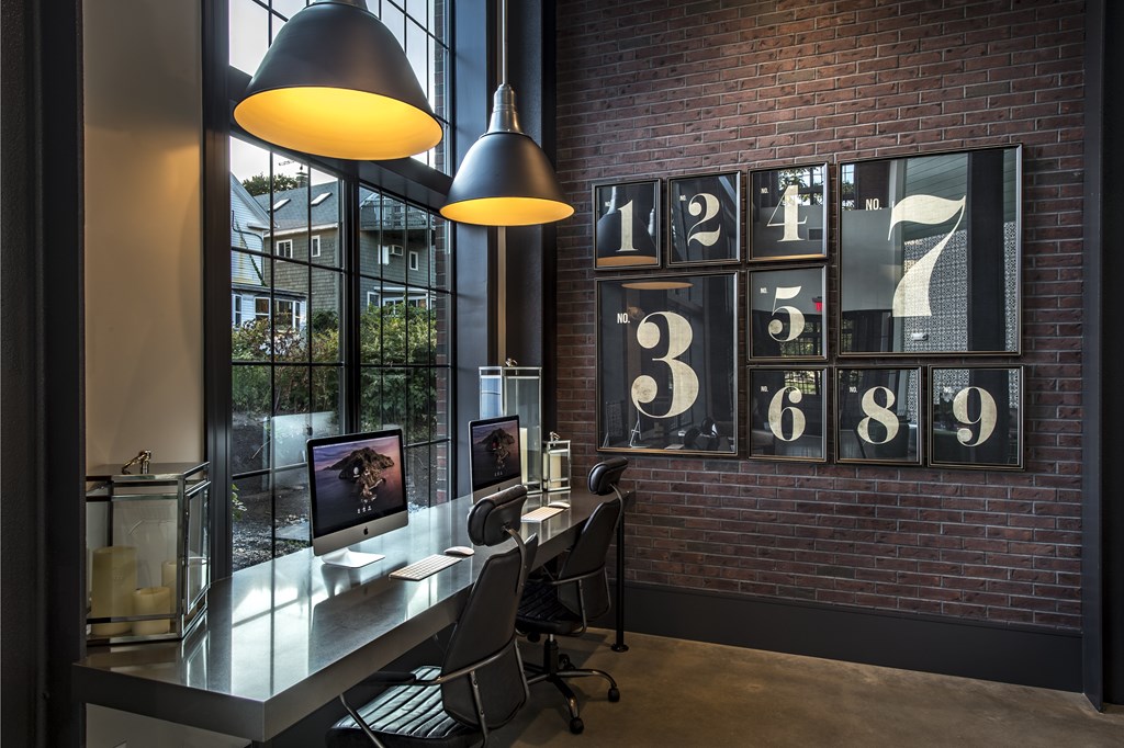 A modern home office with a brick wall and a desk with a computer and chair.