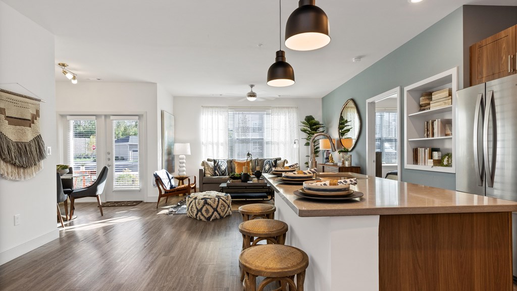Open concept floorplan with kitchen kitchen island and stainless steel refrigerator to the right, living room in background with dining room to the left