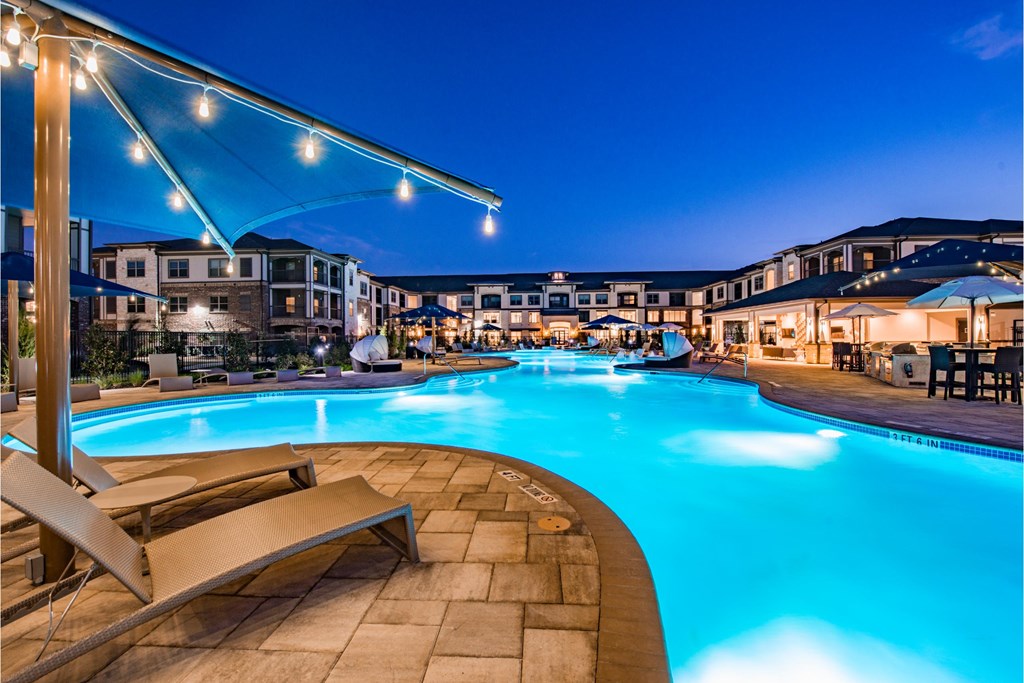 a swimming pool at night with buildings around it