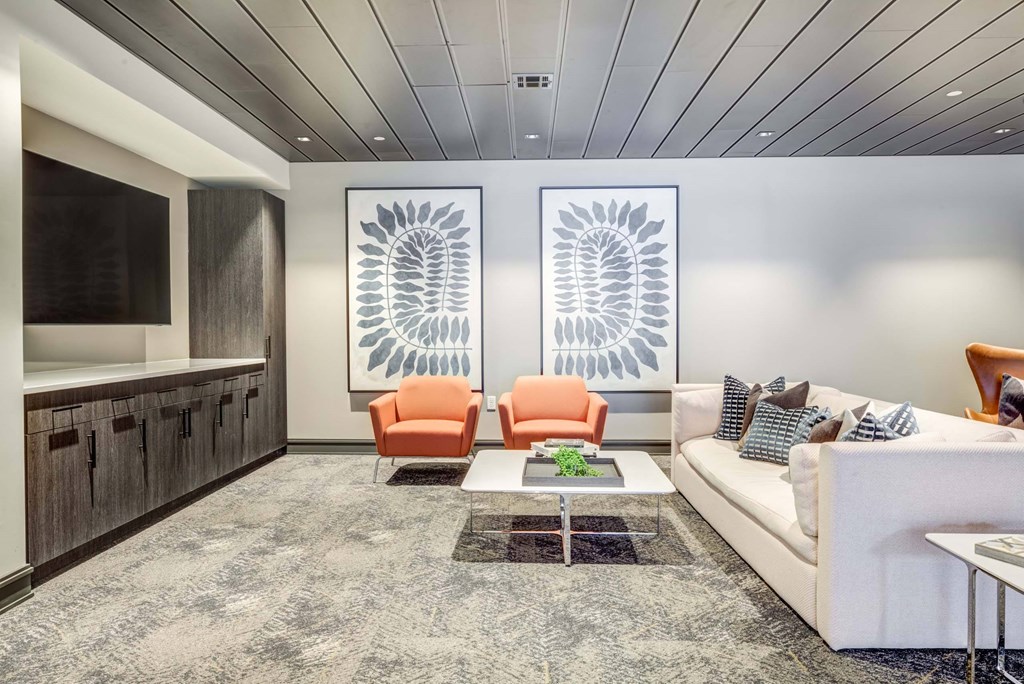 A living room with a white couch, orange chairs, and a grey rug.