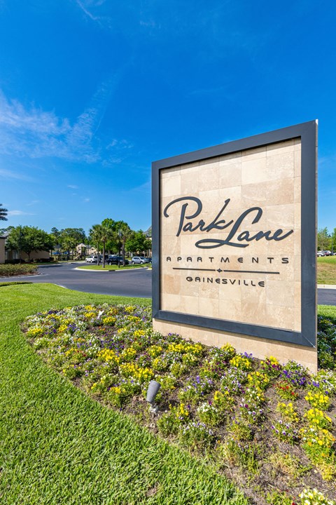 A sign for Park Lane Apartments in Grinesville is shown in front of a blue sky.