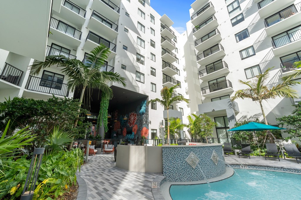 A pool area with a mosaic tile wall and a building in the background.