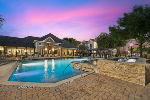 A swimming pool surrounded by a brick patio and a stone wall.