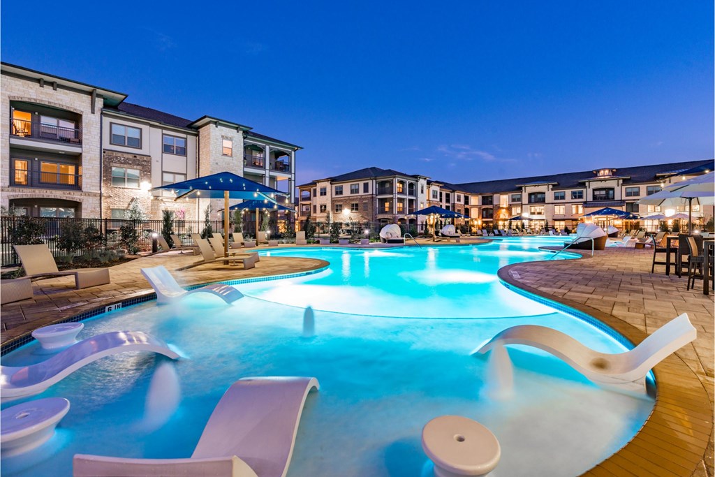 a large swimming pool with chairs and umbrellas at night