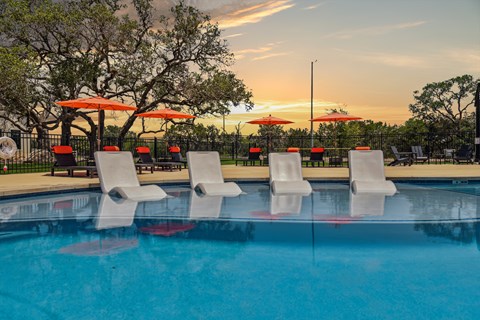 a swimming pool with chairs and umbrellas at sunset