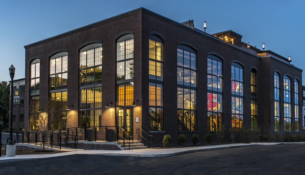 A large brick building with many windows is lit up at dusk.
