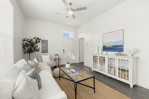 A living room with a white couch, a glass coffee table, and a painting on the wall.