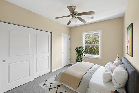 Dog-Friendly Senior Apartments in Blue Springs, MO - The Gardens at Jackson Creek - Bedroom With Ceiling Fan, White Closet Doors, Large Window, Soft Carpet, And Neutral Walls.